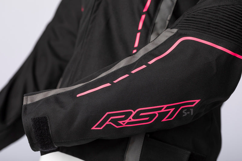 Ärmdetalj på RST Dam Textil Mc-Jacka S-1 med rosa RST-logotyp och reflekterande element för synlighet.